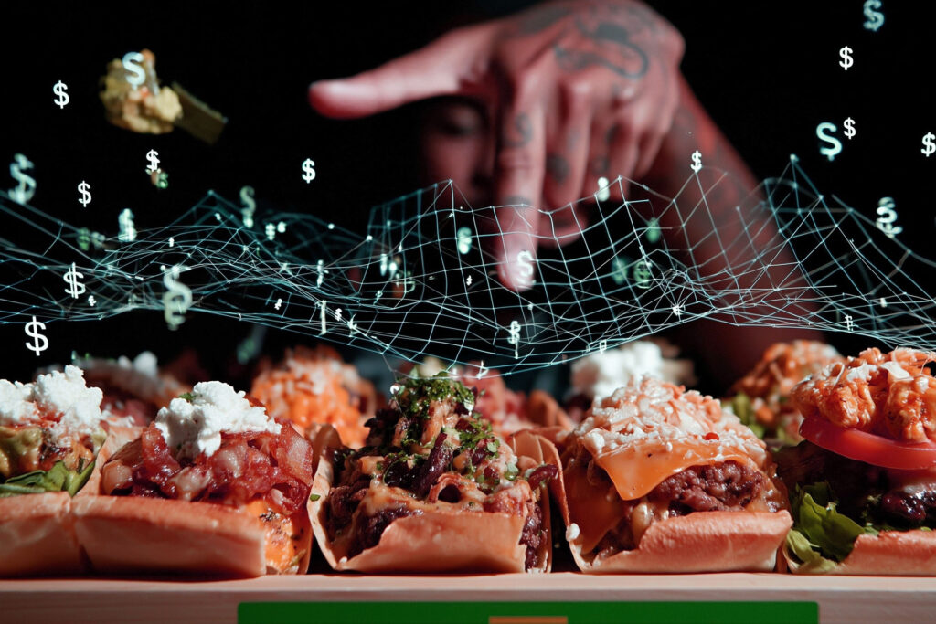 Close-up of gourmet tacos with a tattooed hand above them, overlaid with digital data and floating dollar signs, symbolizing the impact of menu engineering on digital ordering revenue.